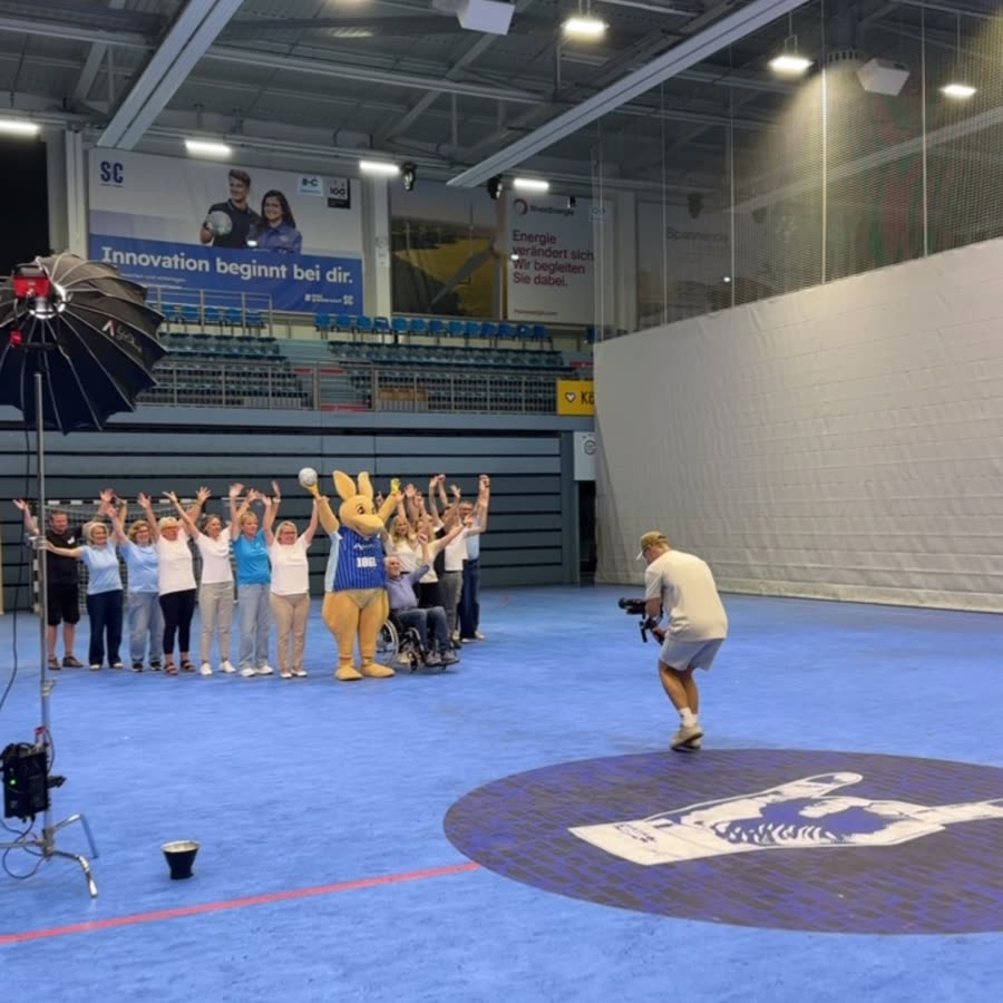 Gruppenaufnahme in einer Sporthalle, unser Kameramann filmt das ganze Team
